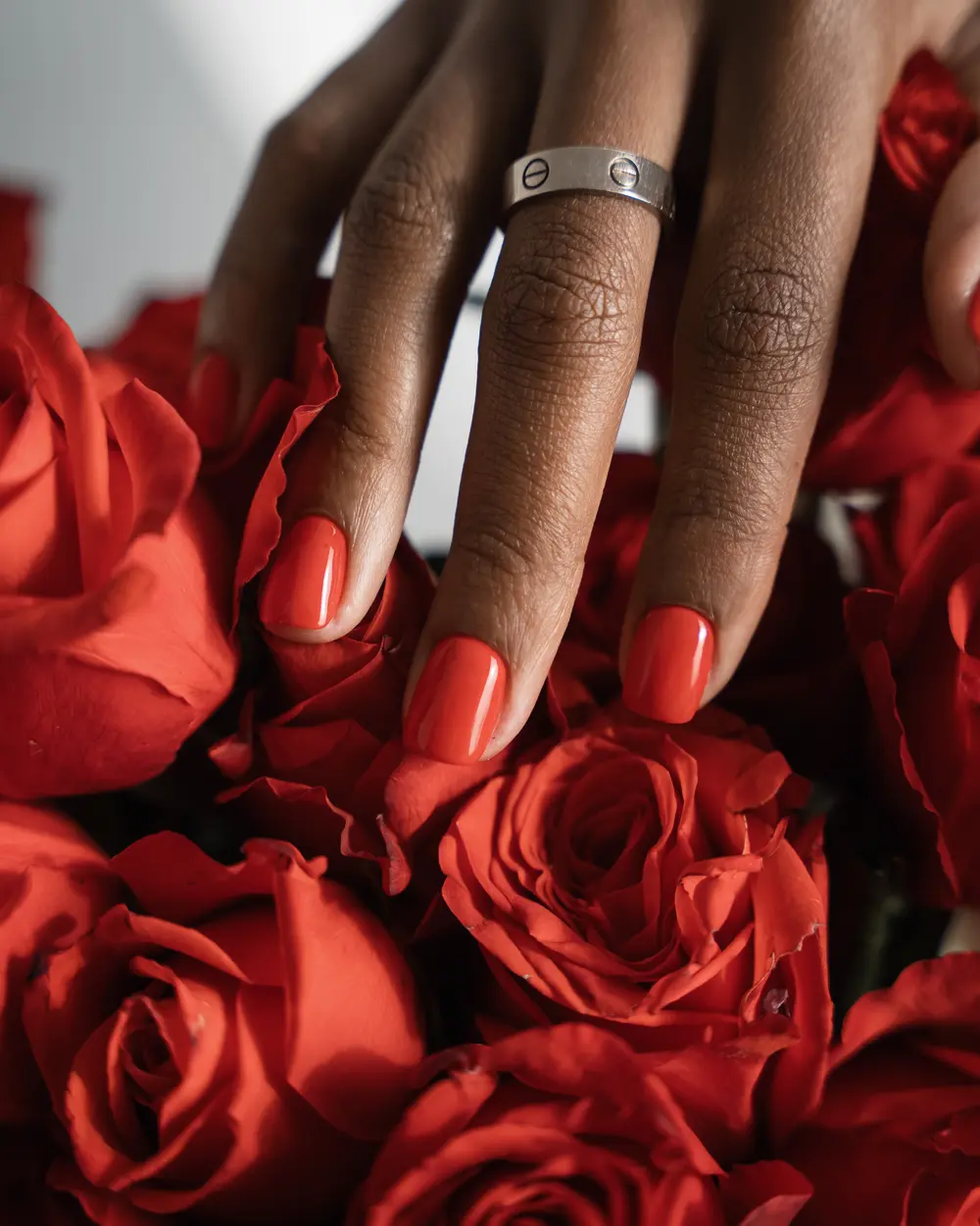 Cherry-red gel manicure resting on a bouquet of red roses